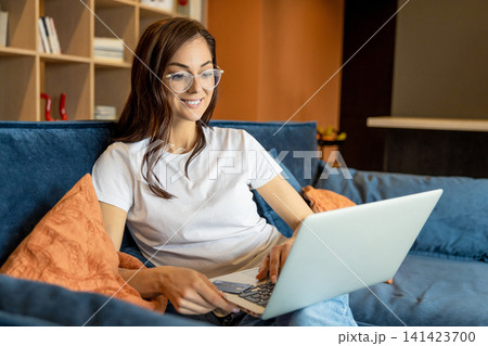 Young woman in eyeglasses working on a laptop and looking busy Young woman in eyeglasses working on a laptop and looking busy 141423700