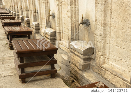 Row of wooden stools and vintage brass water taps for ritual ablution along an ancient stone wall of mosque in Istanbul, Turkey Row of wooden stools and vintage brass water taps for ritual ablution along an ancient stone wall of mosque in Istanbul, Turkey 141423731