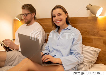 Two young people sitting in the bed and working together Two young people sitting in the bed and working together 141423838