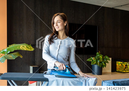 Pretty smiling woman feeling contented while doing ironing Pretty smiling woman feeling contented while doing ironing 141423975