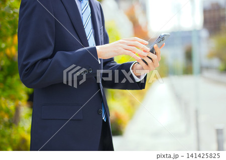屋外でスマホを持つ20代のビジネスマン 屋外でスマホを持つ20代のビジネスマン 141425825