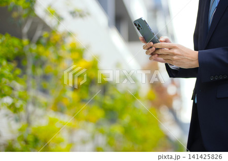 屋外でスマホを持つ20代のビジネスマン 141425826