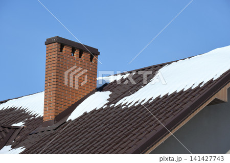 Closeup of house roof top covered with snow in cold winter. Tiled covering of building in wintertime weather Closeup of house roof top covered with snow in cold winter. Tiled covering of building in wintertime weather 141427743