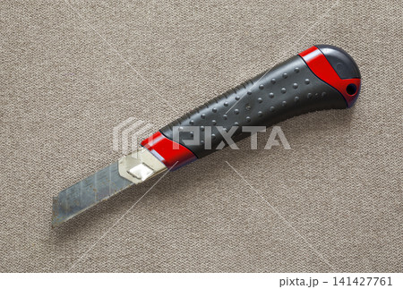 Close-up of isolated stationery retractable metallic knife with sharp blade on light cloth copy space background. Close-up of isolated stationery retractable metallic knife with sharp blade on light cloth copy space background. 141427761