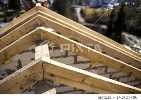 Close-up detail of roof frame of rough wooden lumber beams on background of misty mountain landscape in ecological area. Building, roofing, construction and renovation concept. Close-up detail of roof frame of rough wooden lumber beams on background of misty mountain landscape in ecological area. Building, roofing, construction and renovation concept. 141427786