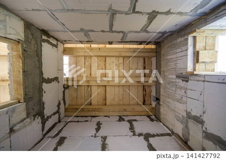 Close-up detail of house room interior under construction and renovation. Energy saving walls of hollow foam insulation blocks, wooden ceiling beams for roof frame. Close-up detail of house room interior under construction and renovation. Energy saving walls of hollow foam insulation blocks, wooden ceiling beams for roof frame. 141427792