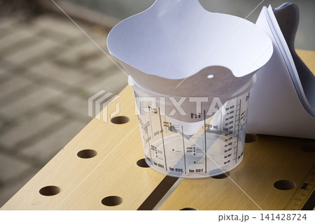 Clear Plastic Measuring Cup With Paper Funnel on Wooden Workbench for Paint Mixing and DIY Projects 141428724