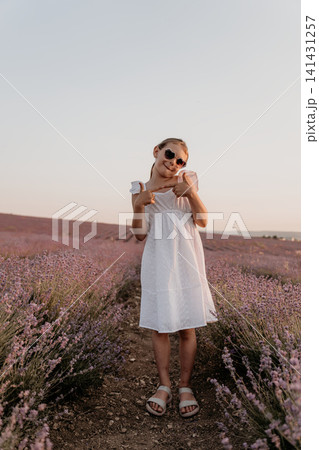 Girl child lavender blooming field meadow wearing white dress and sunglasses having fun enjoying warm summer evening sunshine Girl child lavender blooming field meadow wearing white dress and sunglasses having fun enjoying warm summer evening sunshine 141431257