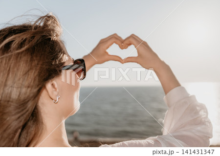 Heart gesture woman ocean framing the bright sky and sea with her hands during a sunny summer day 141431347