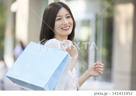ショッピングバックを持って振り返る笑顔の女性 屋外ポートレート 141431952
