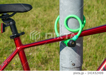 Bicycle secured with bright cable lock to metal pole outdoors for urban theft prevention and commuting Bicycle secured with bright cable lock to metal pole outdoors for urban theft prevention and commuting 141432499