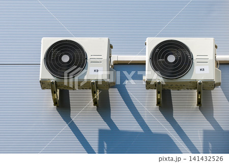 Twin outdoor HVAC air conditioning condenser units mounted on insulated industrial building facade wall 141432526