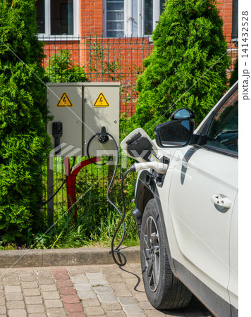 Electric SUV charging at backyard home EV charging station beside private residential property outdoors Electric SUV charging at backyard home EV charging station beside private residential property outdoors 141432528