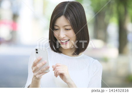 スマートフォンを操作する笑顔の女性 クローズアップ スマートフォンを操作する笑顔の女性 クローズアップ 141432816