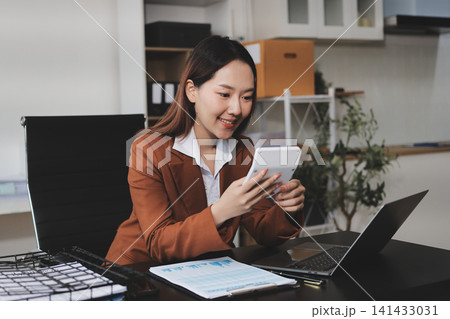 Asian businesswoman using calculator and working on laptop at modern office Asian businesswoman using calculator and working on laptop at modern office 141433031