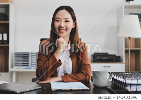 Young Asian professional business woman calculating finances and analyzing data charts on computer, smiling while working on accounting project in a modern office, planning budget Young Asian professional business woman calculating finances and analyzing data charts on computer, smiling while working on accounting project in a modern office, planning budget 141433046
