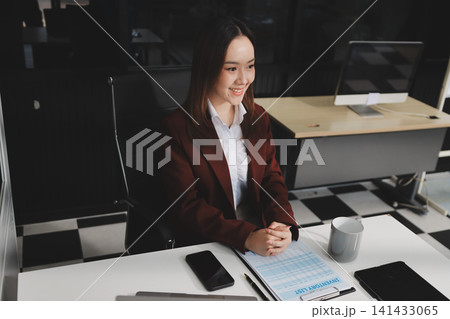 Smiling asian businesswoman talking on phone and using laptop while working at office desk Smiling asian businesswoman talking on phone and using laptop while working at office desk 141433065