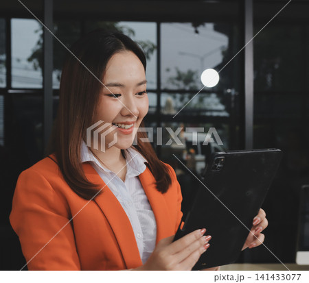 Smiling asian businesswoman talking on phone and using laptop while working at office desk Smiling asian businesswoman talking on phone and using laptop while working at office desk 141433077