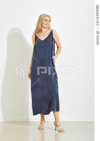 Woman wearing long dress standing against white wall in indoor space 141434496