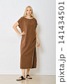 Woman in brown dress with high slit standing in studio with white wall 141434501
