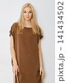 Blonde woman in brown dress standing in studio against white wall 141434502
