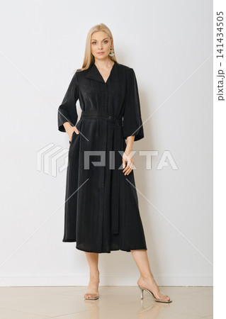 Woman posing in black dress with sleeves and belt in indoor studio setting Woman posing in black dress with sleeves and belt in indoor studio setting 141434505