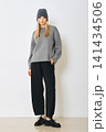 Woman wearing gray sweater, knitted hat and black pants in indoor setting 141434506
