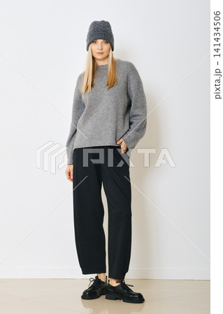 Woman wearing gray sweater, knitted hat and black pants in indoor setting Woman wearing gray sweater, knitted hat and black pants in indoor setting 141434506