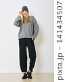 Woman in gray sweater and black pants poses indoors with playful expression 141434507