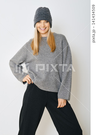 Woman wearing grey sweater and hat posing in studio with simple background Woman wearing grey sweater and hat posing in studio with simple background 141434509