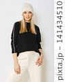 Woman in black sweater and white pants with knitted hat in indoor setting 141434510
