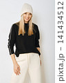 Woman wearing black sweater and white pants standing against light background 141434512