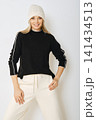 Woman posing in black sweater and white pants with knit hat 141434513