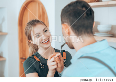 Happy couple cooking together in a cozy kitchen, sharing food and smiling Happy couple cooking together in a cozy kitchen, sharing food and smiling 141434554
