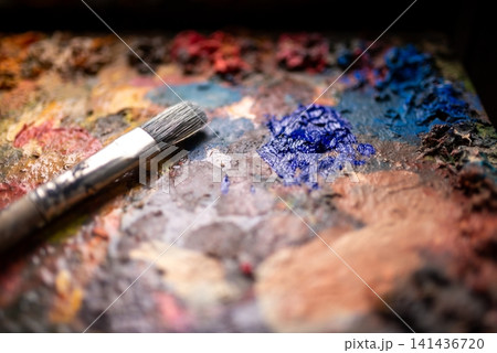 Close-up of used paintbrush resting on textured artist palette with mixed oil paints and vivid Close-up of used paintbrush resting on textured artist palette with mixed oil paints and vivid 141436720