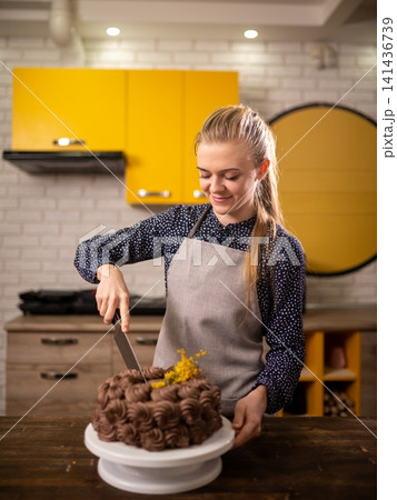 Young woman in modern kitchen stirring chocolate truffles on cake stand under warm lighting 141436739