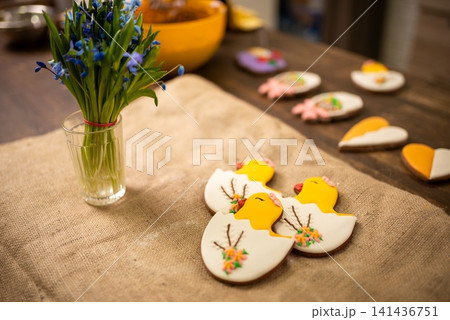 Handmade iced cookies shaped like chicks and eggs on rustic linen table with spring floral bouquet Handmade iced cookies shaped like chicks and eggs on rustic linen table with spring floral bouquet 141436751