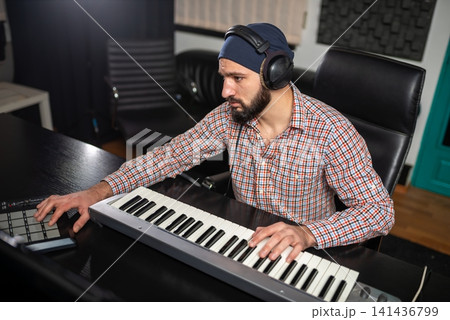 Man composing music at studio keyboard with headphones Man composing music at studio keyboard with headphones 141436799