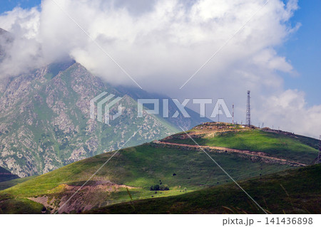 Mountain range with green hills and communication towers under cloudy sky Mountain range with green hills and communication towers under cloudy sky 141436898