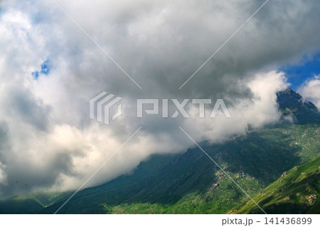 Clouds drift over jagged peaks, green valleys below Clouds drift over jagged peaks, green valleys below 141436899