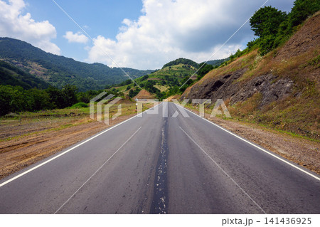 Empty asphalt road between rolling hills under bright sky 141436925