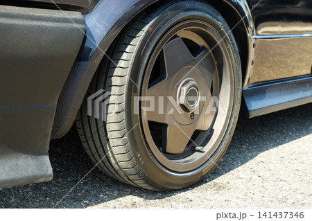 Close up detail view of a modern performance car wheel and tire on a dark blue vehicle with custom body kit, showcasing automotive tuning and design 141437346