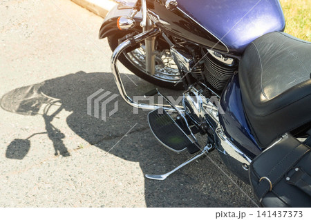 Purple cruiser motorcycle parked on asphalt road during day, sun creating strong shadow, detailed view of chrome engine parts, footboards, and leather seat, side view of vehicle. Purple cruiser motorcycle parked on asphalt road during day, sun creating strong shadow, detailed view of chrome engine parts, footboards, and leather seat, side view of vehicle. 141437373