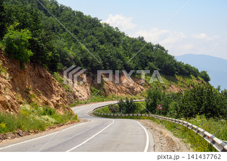 Winding mountain road surrounded by dense trees and guardrails Winding mountain road surrounded by dense trees and guardrails 141437762