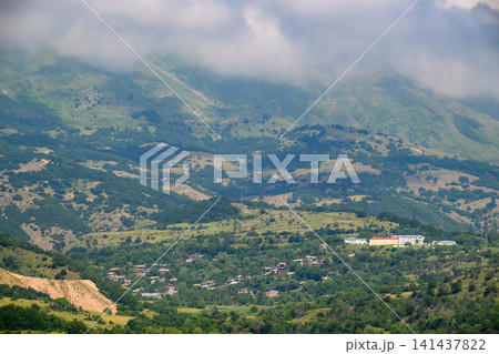 Green mountain landscape with village and misty clouds 141437822
