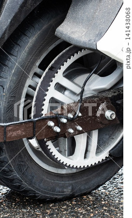 Close-up of motorcycle rear wheel and drive belt system, showing mechanical detail of custom brown component secured by bolts and zip ties on wet asphalt surface Close-up of motorcycle rear wheel and drive belt system, showing mechanical detail of custom brown component secured by bolts and zip ties on wet asphalt surface 141438068