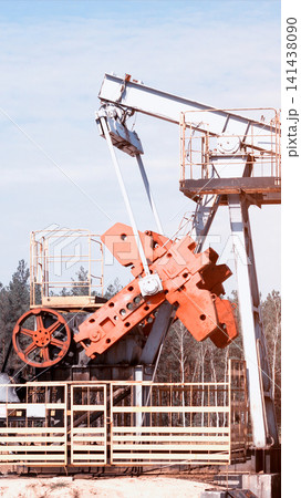 Oil pumpjack machinery detail on an oil field with forest background under pale sky, showcasing metal beams and counterweights of the extraction equipment, nobody present, vertical photo Oil pumpjack machinery detail on an oil field with forest background under pale sky, showcasing metal beams and counterweights of the extraction equipment, nobody present, vertical photo 141438090