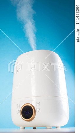 White electric humidifier operating, emitting visible stream of water vapor into air, digital display showing current room temperature and humidity level, modern home appliance, vertical photo White electric humidifier operating, emitting visible stream of water vapor into air, digital display showing current room temperature and humidity level, modern home appliance, vertical photo 141438094