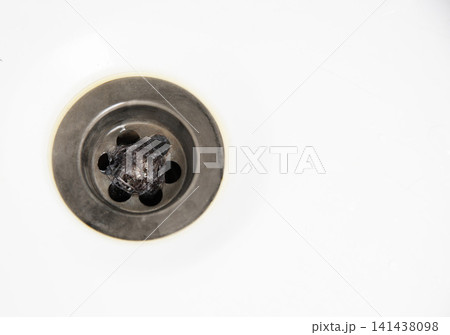 Close-up view of dark hair mass caught in metallic drain of white bathroom sink causing plumbing obstruction problem home maintenance issue needing repair, copy space Close-up view of dark hair mass caught in metallic drain of white bathroom sink causing plumbing obstruction problem home maintenance issue needing repair, copy space 141438098