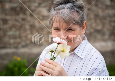 Senior woman holding flowers and smiling in a serene garden setting. Mindfulness horticultural therapy and healthy aging wellbeing 141438112